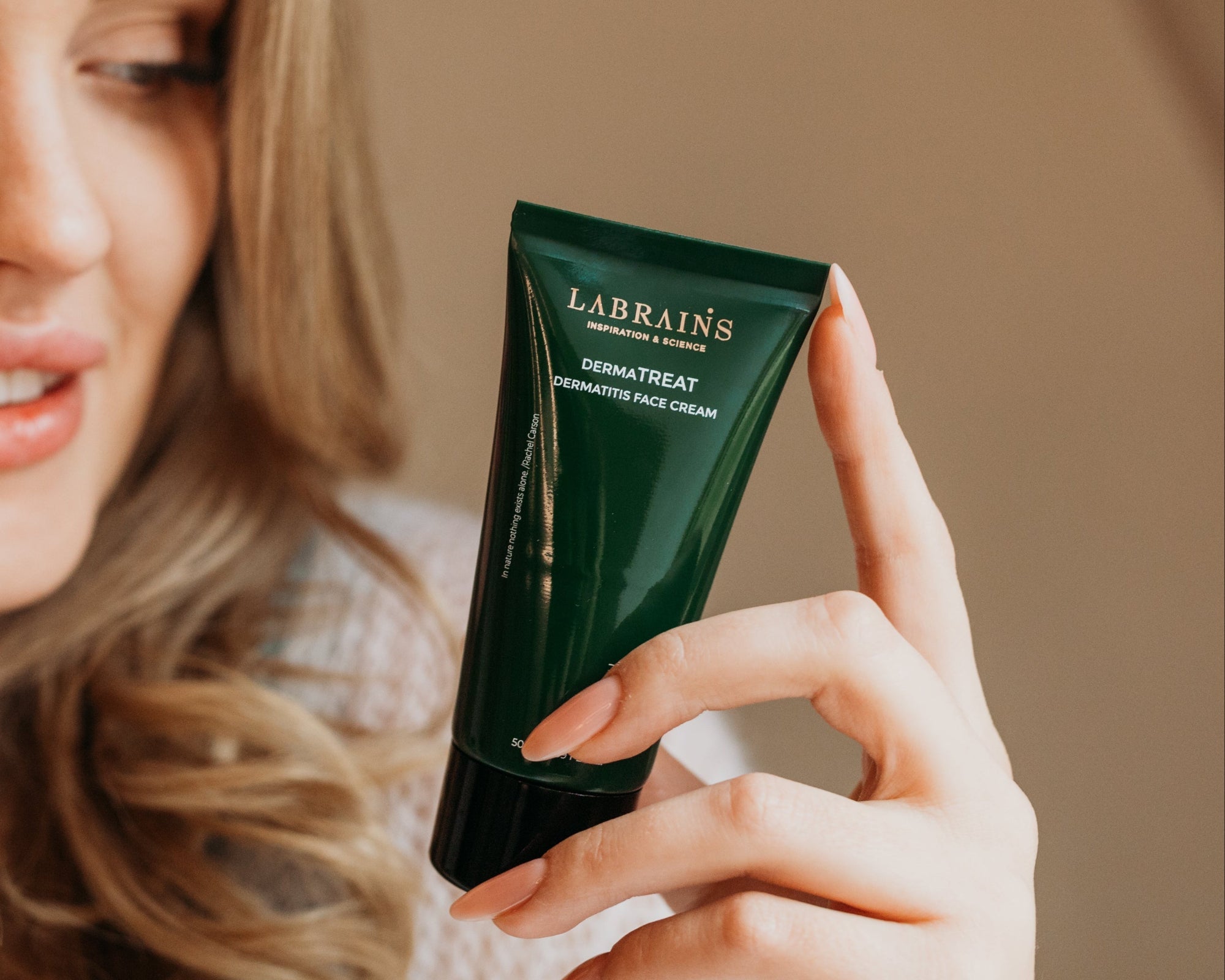 woman holding a green tube of Labrains Dermatreat cream against a neutral background