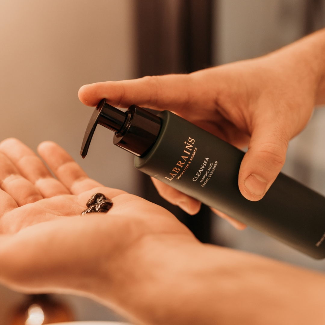 man holding labrains nordic mud cleansing gel pump bottle and squeezing the black product in his hands