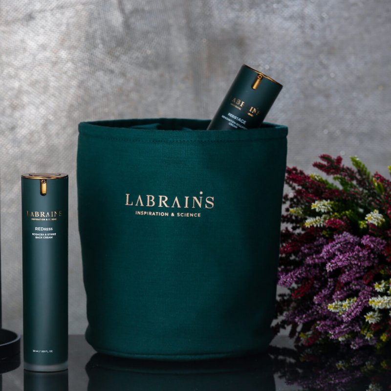 An elegant green labrains cosmetic bag with the brand name in golden letters, displayed alongside a floral arrangement and a labrains skincare bottle.