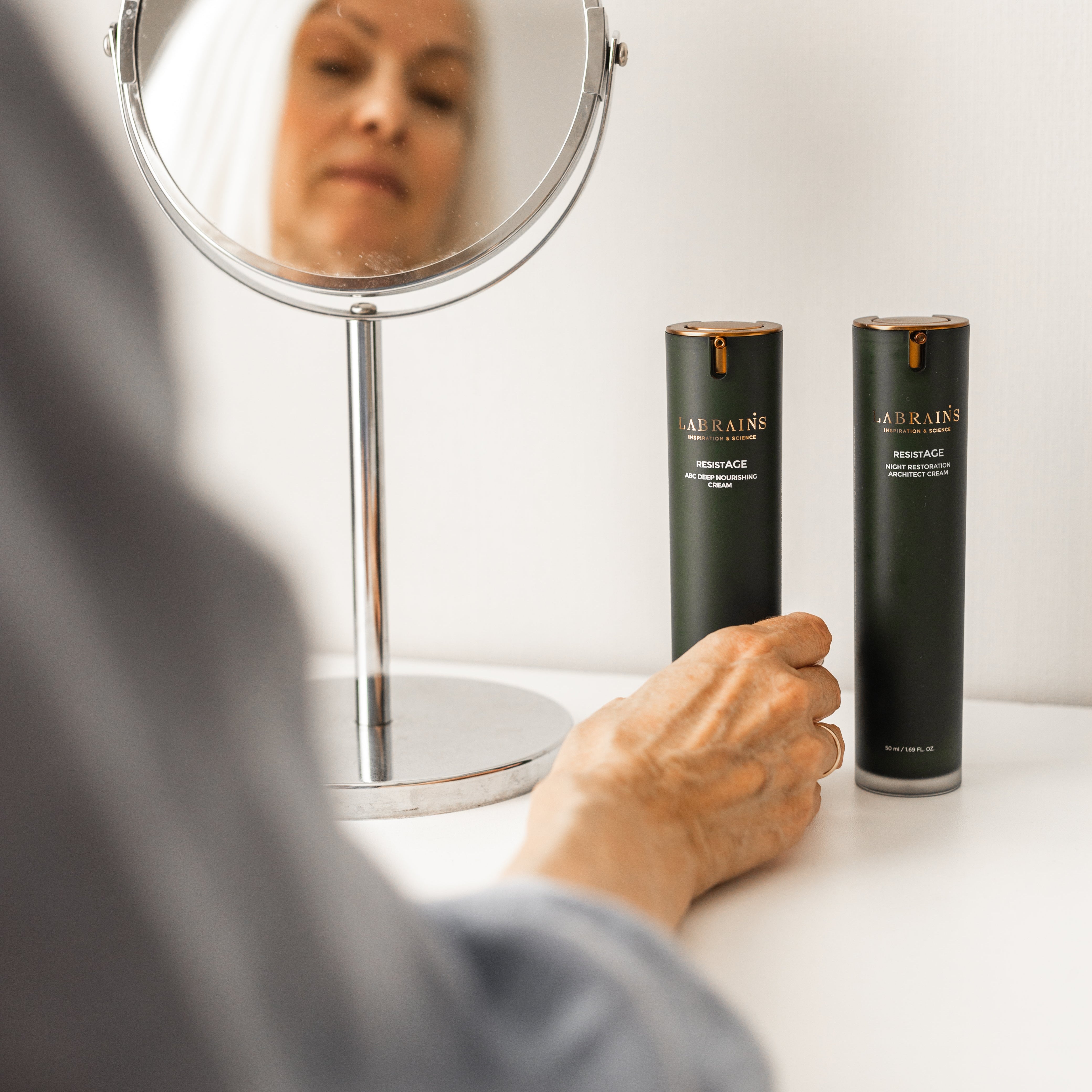 Woman looking in a mirror with two labrains resistage skincare products on a table.