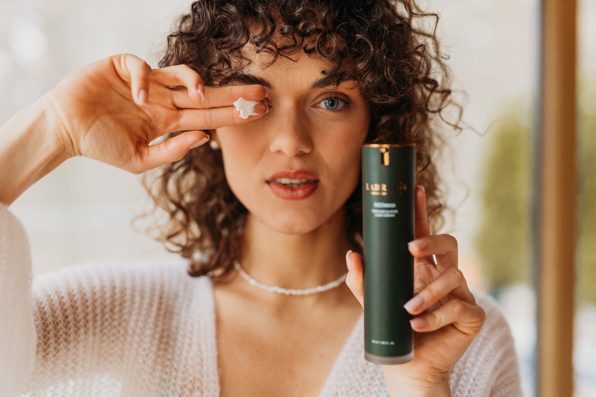 curly woman applying labrains cream to her face with the product in hand