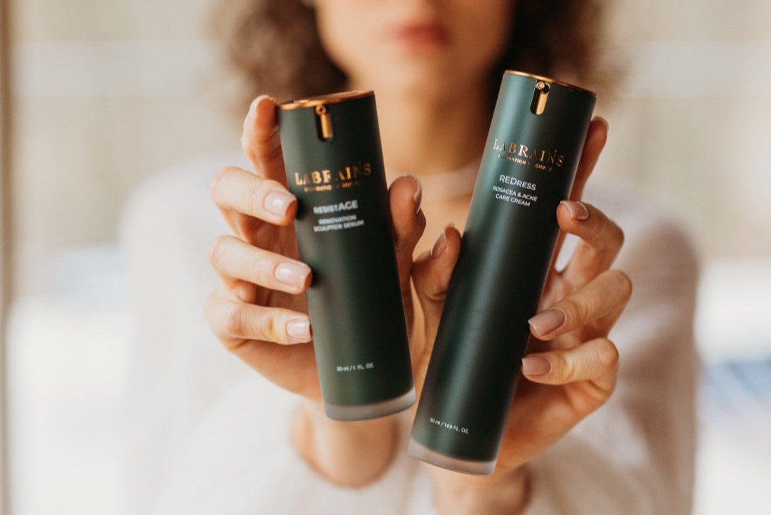 Two dark green labrains skincare bottles held by a woman with a blurred background