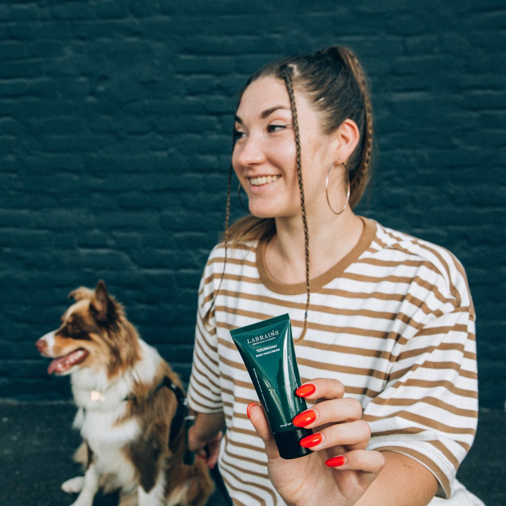teenage girl in striped shirt holding a green tube of labrains cream youngdali with a dog in the background