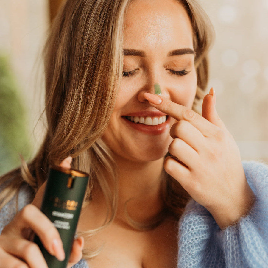 Smiling woman holding LABRAINS Rosa Cease Care Serum and applying green serum to her nose
