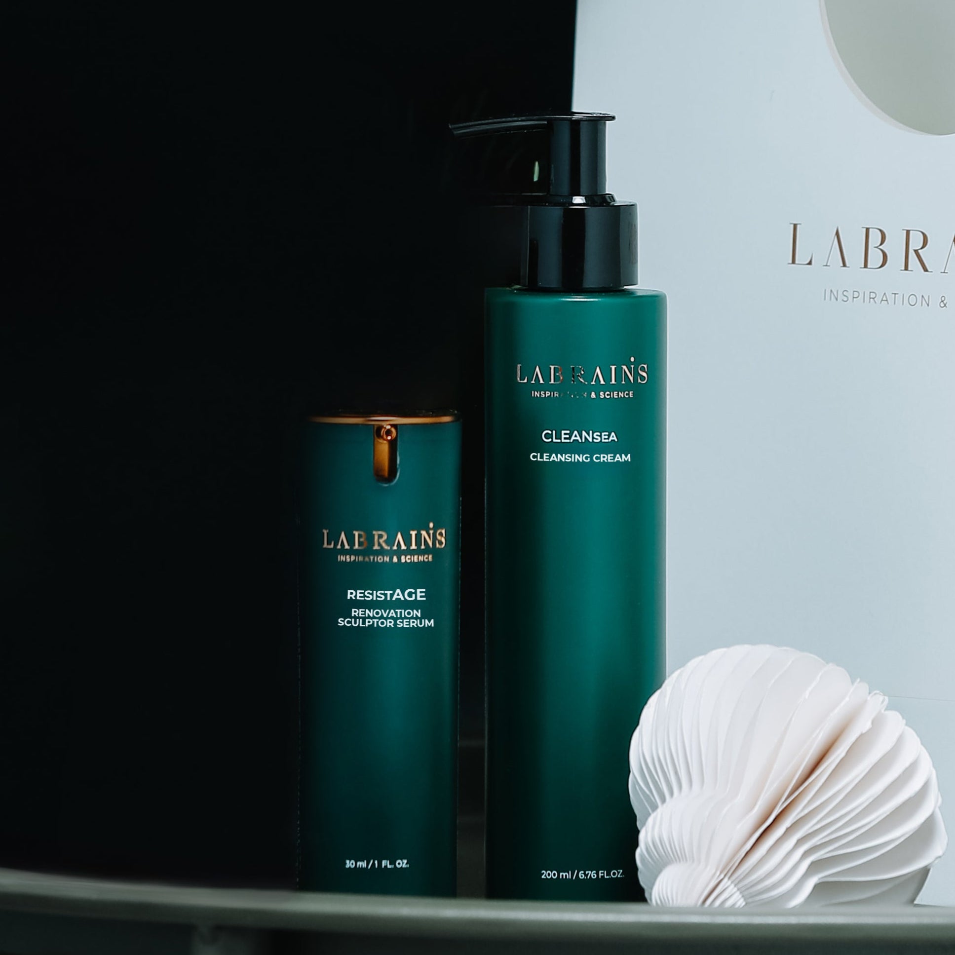 LABRAINS skincare products, renovation sculptor serum and cleansing cream, on a dark surface with a white box in the background