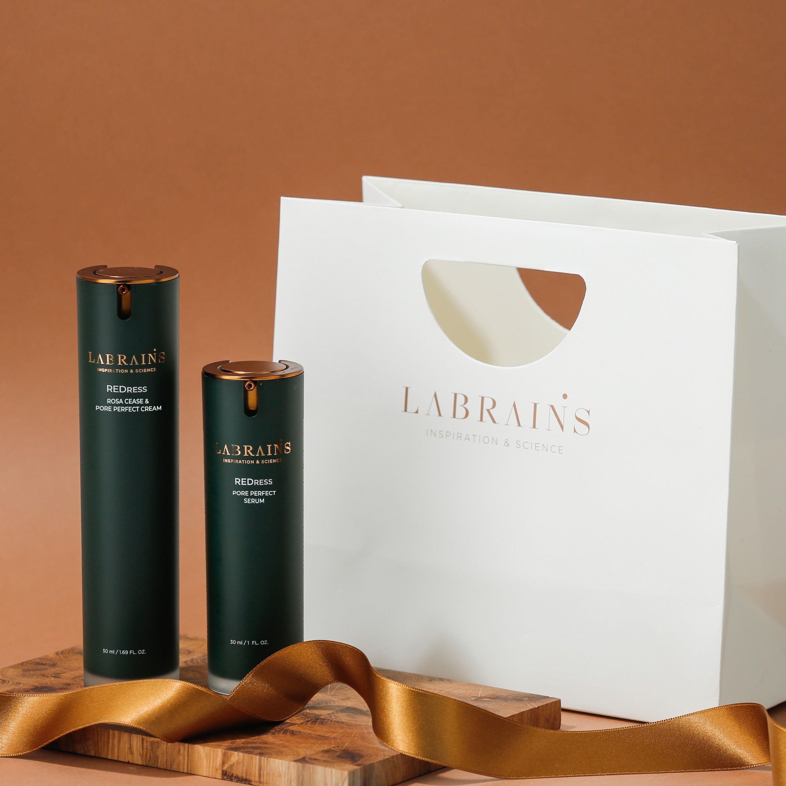 Two green skincare bottles by labrains next to a white gift bag on a wooden surface with a brown background.